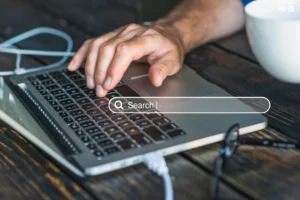 A person typing on a laptop keyboard with a digital overlay of Google's AI-powered search box.